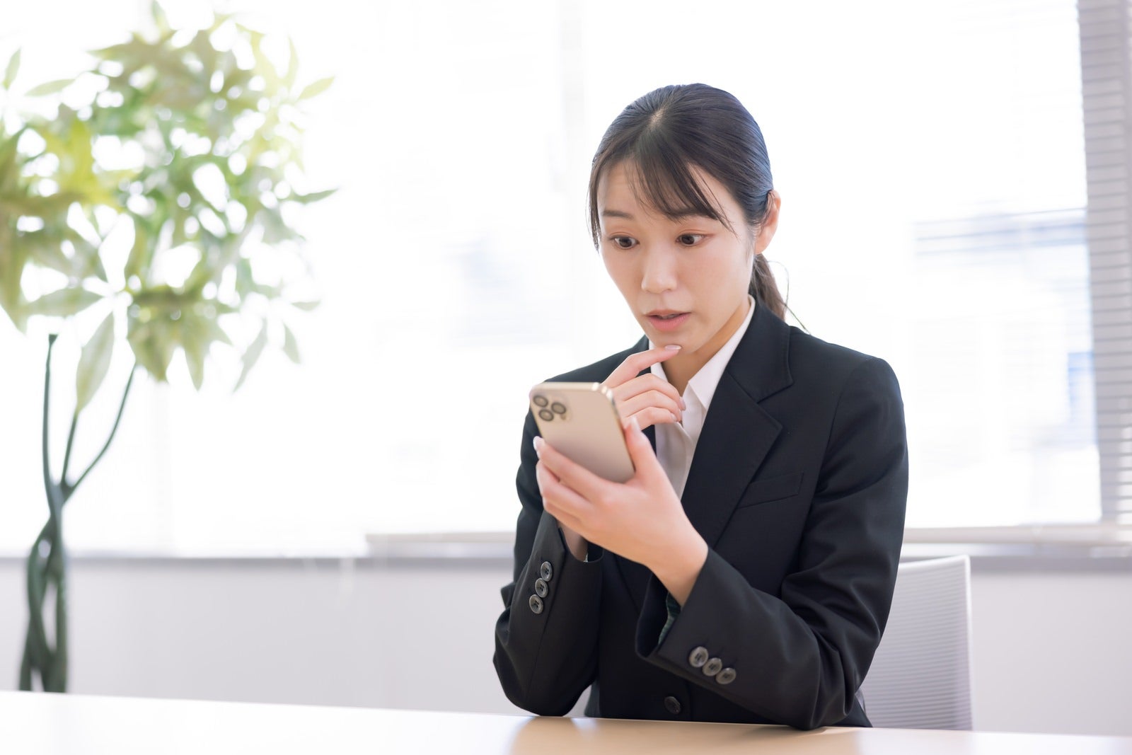 「スマホを見て驚く女性事務員」の写真［モデル：SAKI］