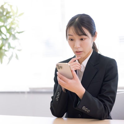 スマホを見て驚く女性事務員の写真
