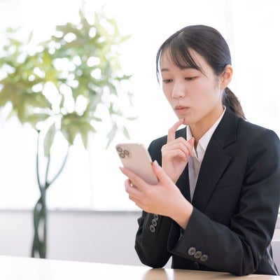 スマホの画面を見ながら真剣に悩む女性オフィスの写真