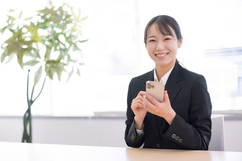 スマホを持って笑顔のスーツ姿の女性