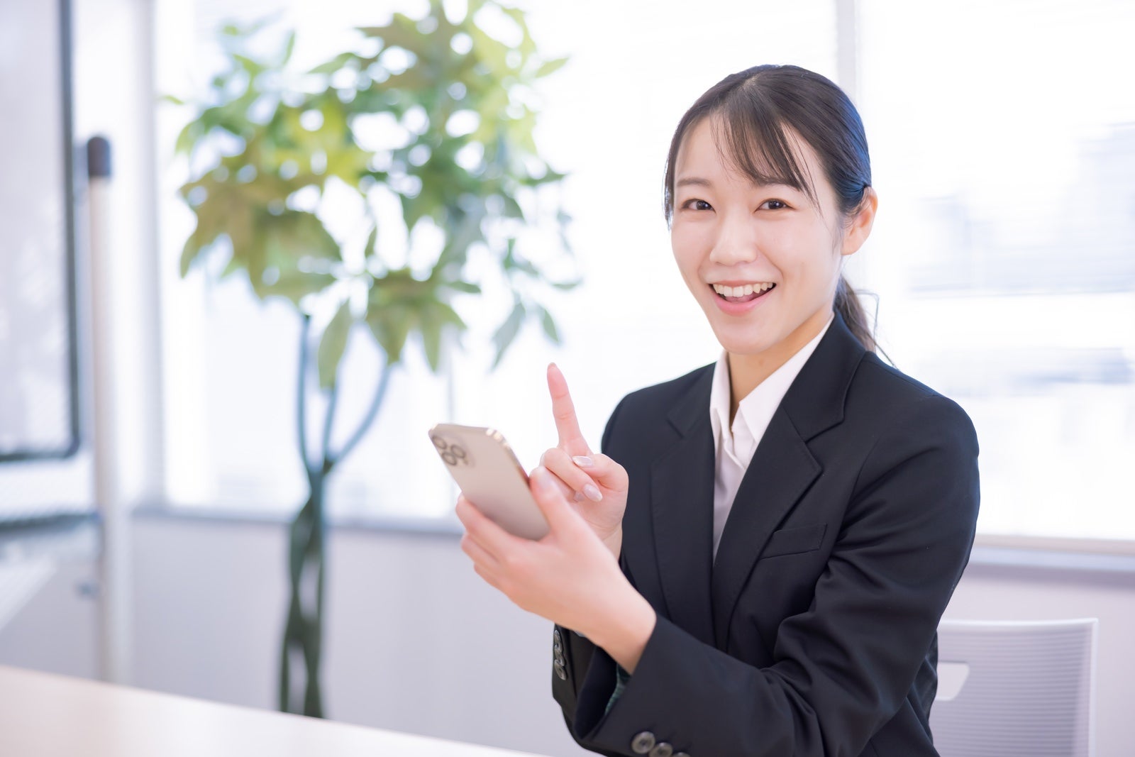 黒いスーツでスマートフォンを持ち笑顔の女性［モデル：SAKI］