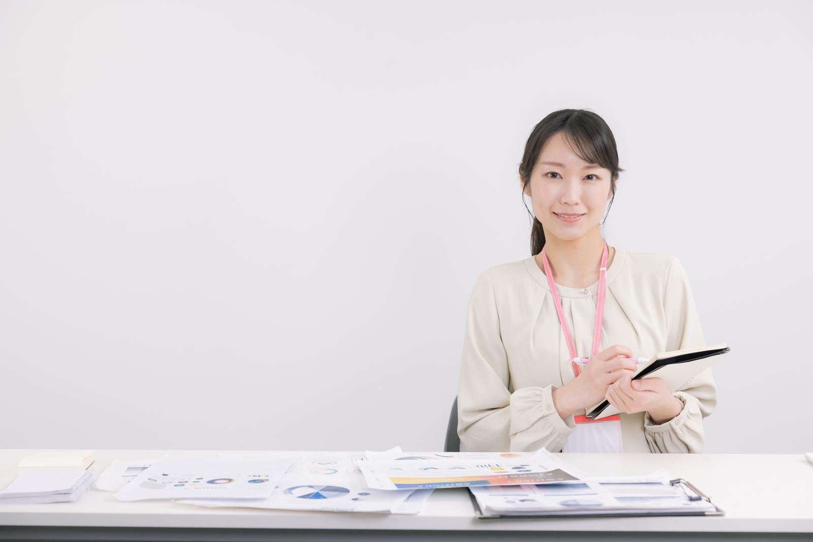 「デスク上の書類と議事録を取る事務の女性」の写真［モデル：SAKI］