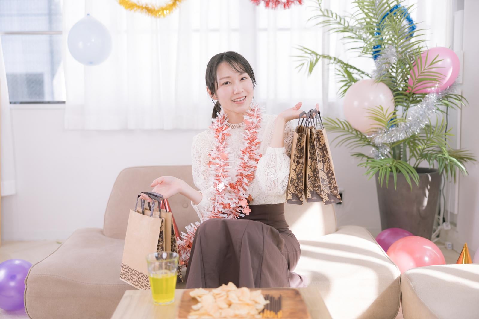 「パーティーのでたくさんのプレゼント袋を両手に持つ女性」の写真［モデル：SAKI］