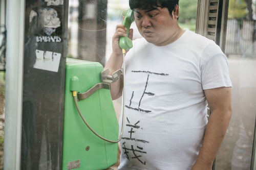 公衆電話から匿名のタレコミをする男性の写真