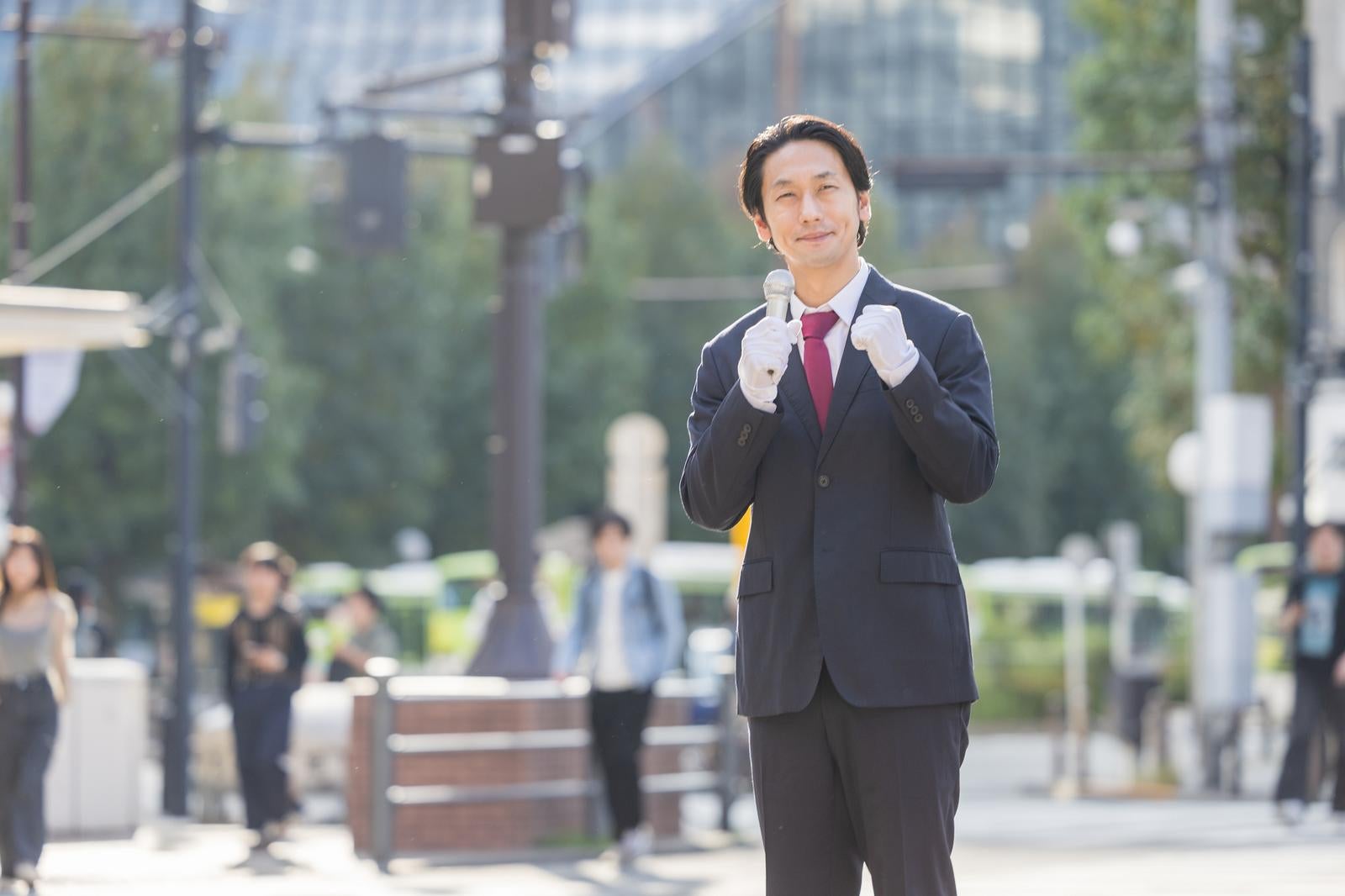 「歩行者の多い駅前で有権者に訴える政治家風の男性」の写真［モデル：大川竜弥］