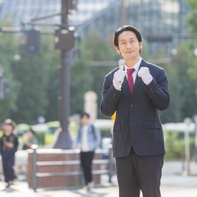 歩行者の多い駅前で有権者に訴える政治家風の男性の写真