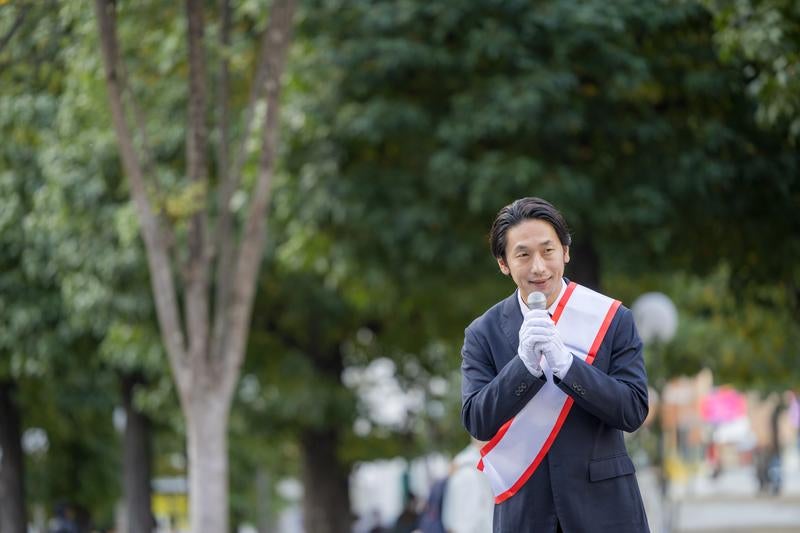 緑豊かな公園で演説する若い男性政治家の写真