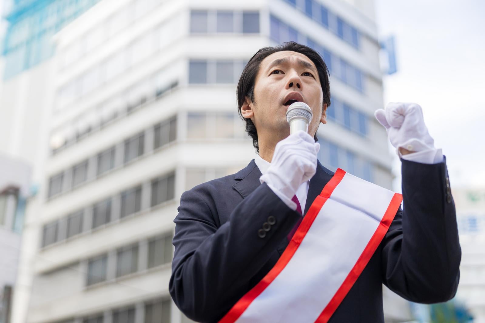 「たすきを着けて街頭演説をする40代男性」の写真［モデル：大川竜弥］