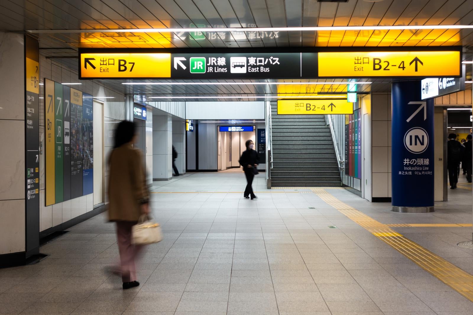 渋谷駅地下通路のJR線・井の頭線方面の黄色い案内板と歩く通行人