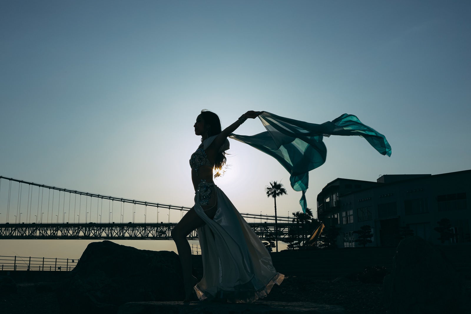 夕暮れの海岸で布をはためかせながら踊る女性のシルエット［モデル：モデルリリース］