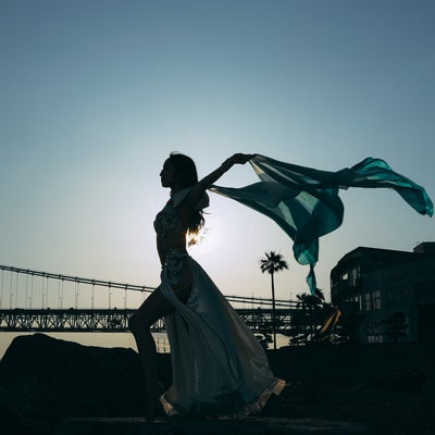 夕暮れの海岸で布をはためかせながら踊る女性のシルエットの写真
