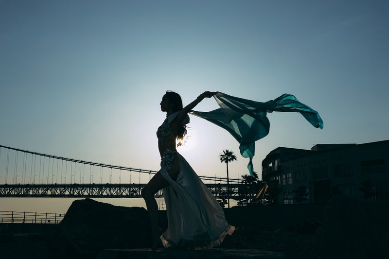 夕暮れの海岸で布をはためかせながら踊る女性のシルエット