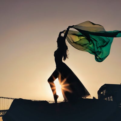 夕日を背に翻る布をはためかせながら踊るダンサーの写真