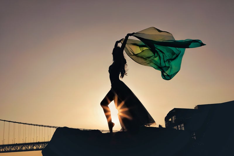 夕日を背に翻る布をはためかせながら踊るダンサーの写真