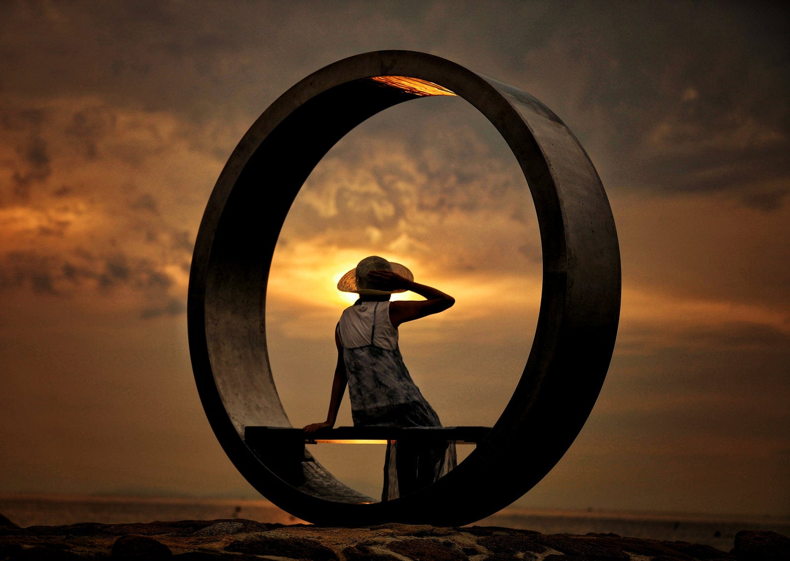 「夕暮れとリング状のオブジェに腰掛ける女性」の写真［モデル：モデルリリース］