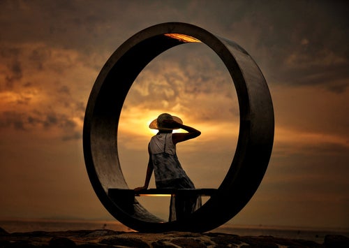 夕暮れとリング状のオブジェに腰掛ける女性の写真