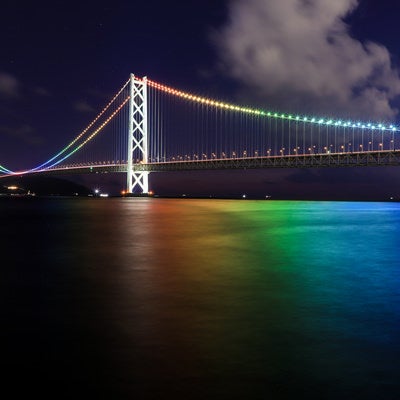レインボーカラーにライトアップした海と明石海峡大橋の写真