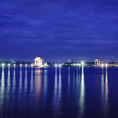 海に伸びる工場夜景の光の写真