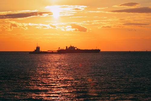 夕焼けに染まるさざ波と船のシルエットの写真
