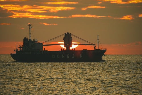 夕日と重なる貨物船の写真