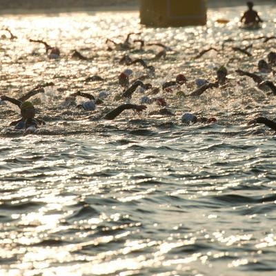 水面に光る日と競泳するトライアスロン選手の写真