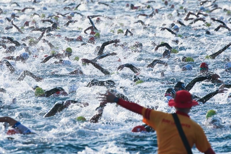 トライアスロン競技で泳ぐ選手たちと監視員の写真