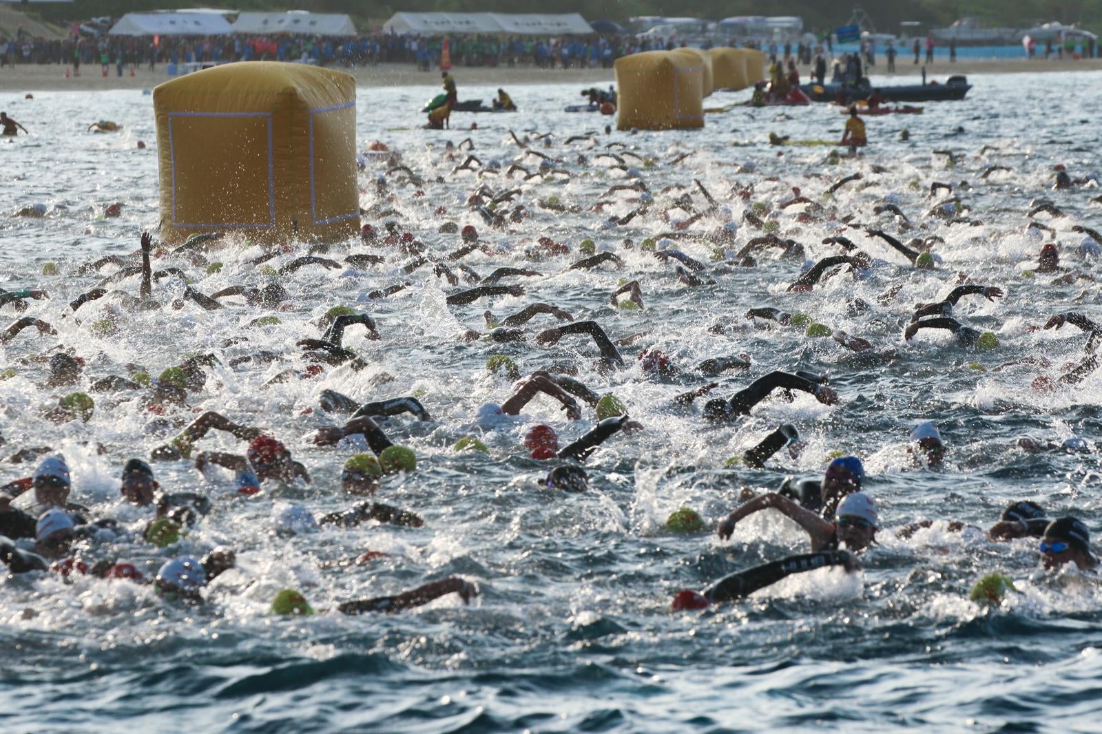 「水しぶきを上げて競い合うトライアスロン選手たち」の写真