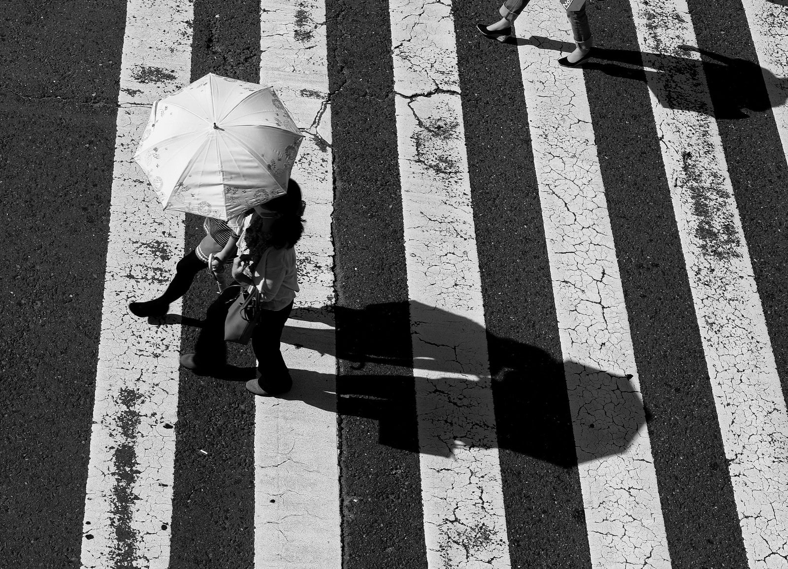 「横断歩道を渡る日傘を差したカップル」の写真
