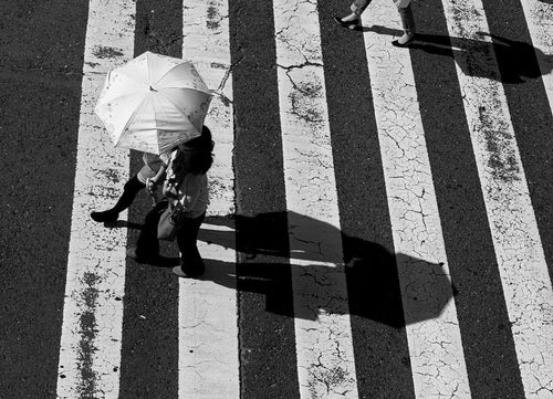 横断歩道を渡る日傘を差したカップルの写真