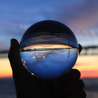ガラス玉越しに見た夕焼けと橋の写真