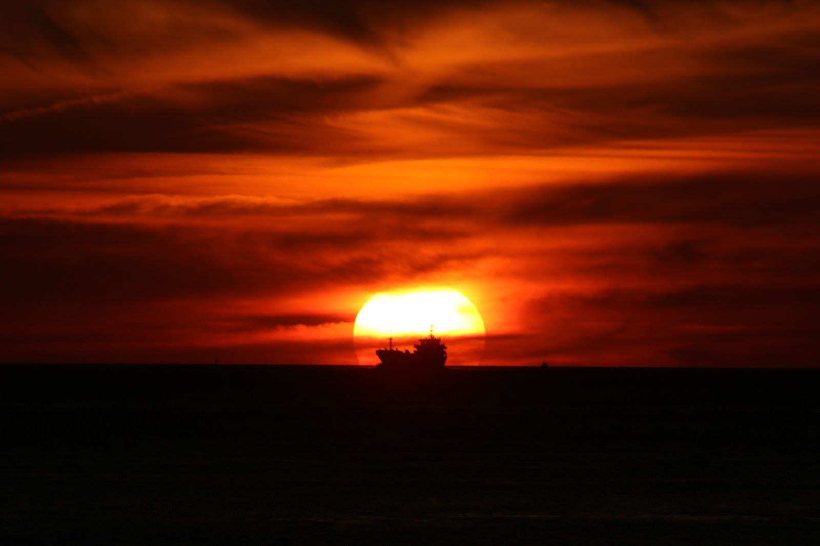 「夕日に染まる空と貨物船のシルエット」の写真