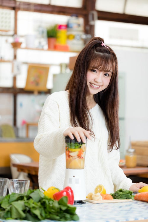 ミキサーに野菜や果物を入れてスムージーを作る女子の写真