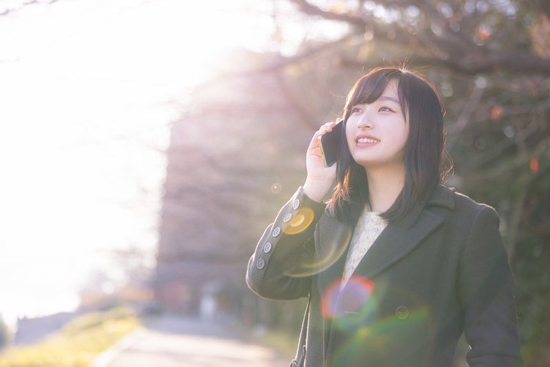 樹木に囲まれた屋外で携帯電話をかける女性の待ち合わせ風景の写真