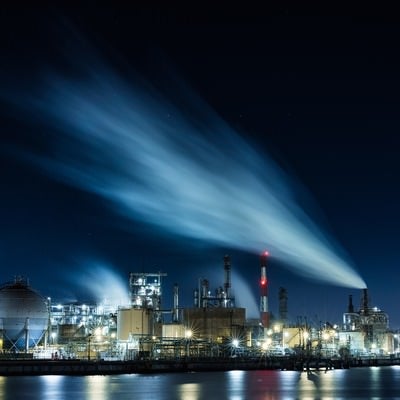 夜空に流れる煙と工場夜景の写真