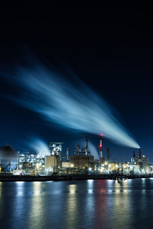 夜空に流れる煙と工場夜景の写真