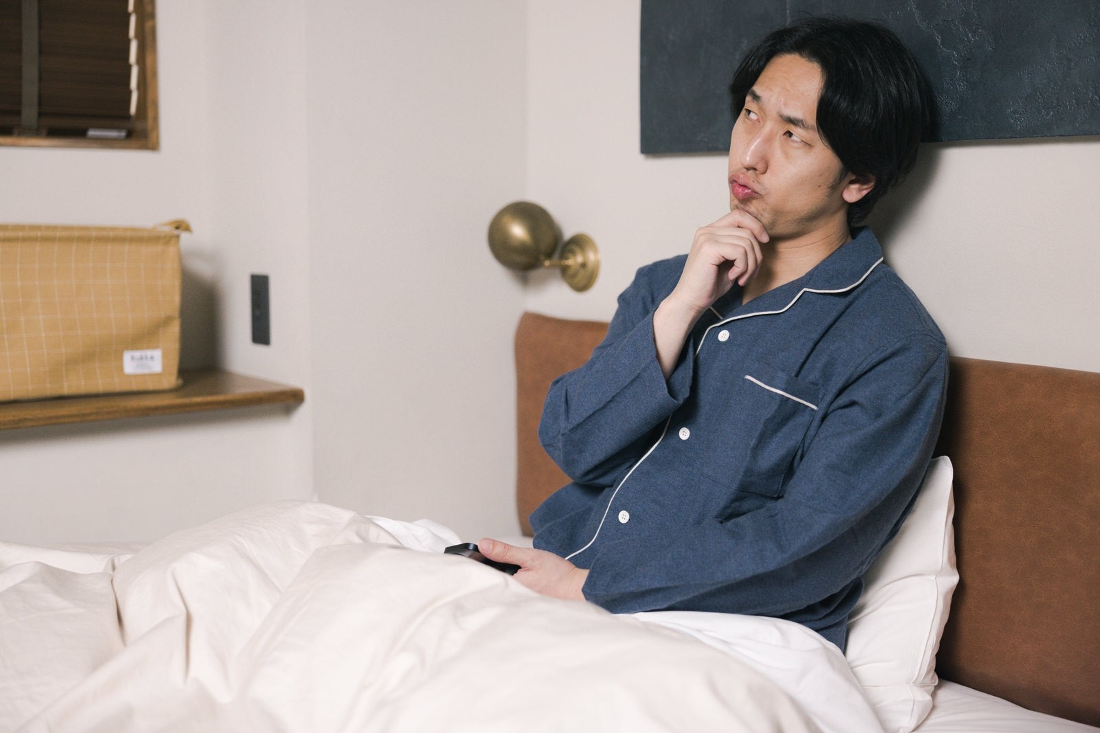 「ベッドの上で一考する男性」の写真［モデル：大川竜弥］