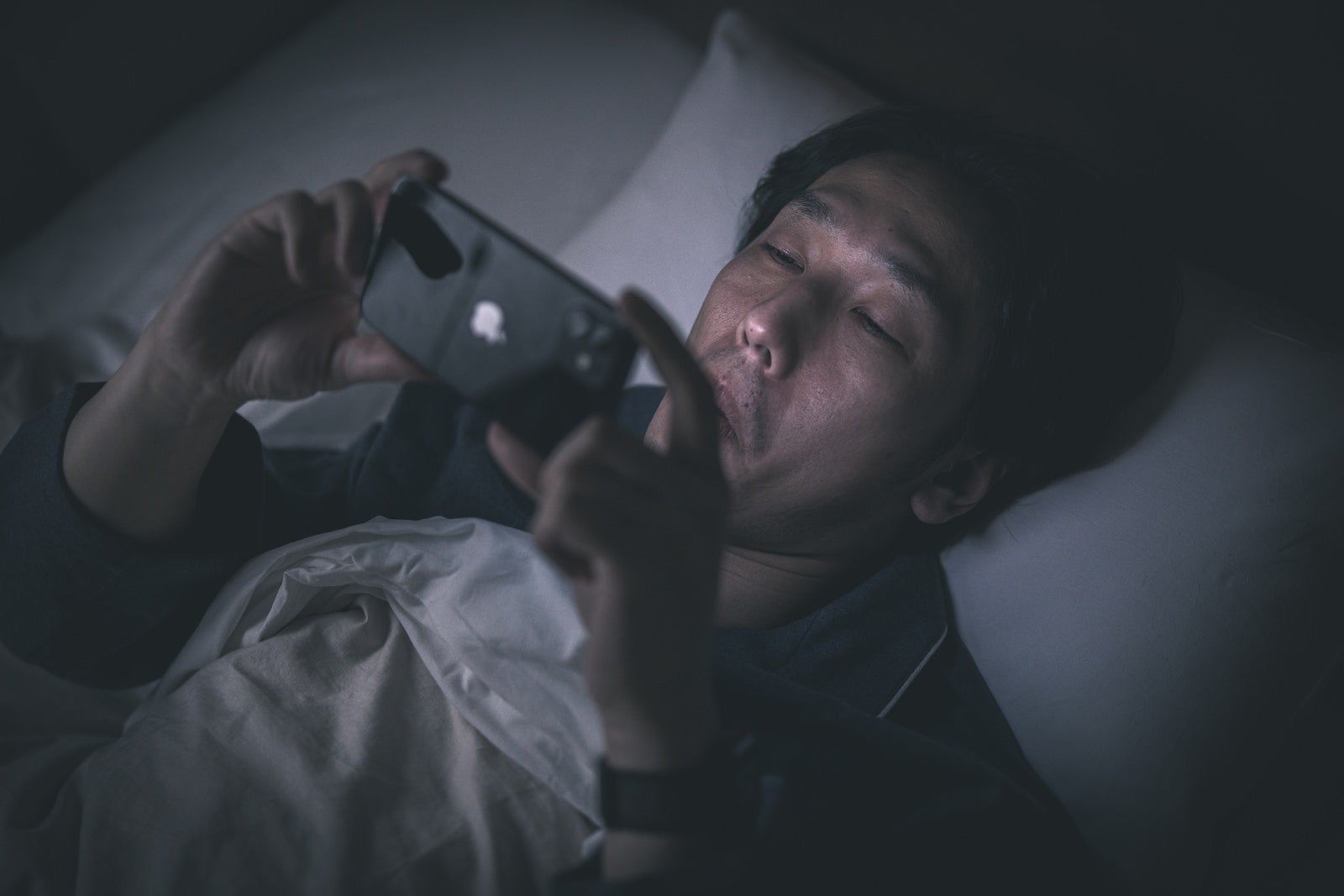 「暗闇の中ベッドでスマホを見る男性」の写真［モデル：大川竜弥］