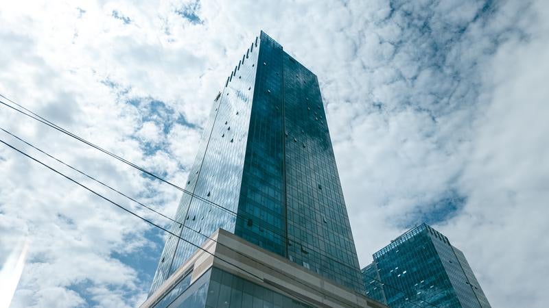 青空と雲を背景にした現代的なガラス張り高層オフィスビルの写真