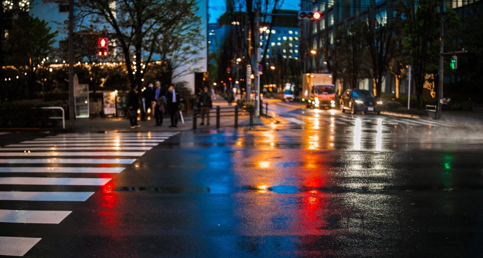 雨に濡れた夕暮れの横断歩道に信号や街灯の光が反射しているローアングルの写真