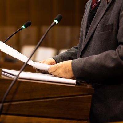 マイクを前に資料を読み上げる男性市議会議員の写真