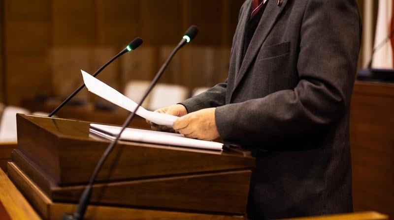 マイクを前に資料を読み上げる男性市議会議員の写真