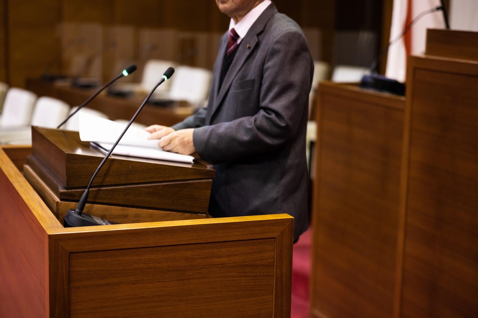 「本会議場でマイクに向かう市議」の写真