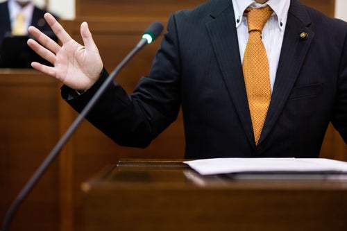 議会の動揺を抑えようとする議員の手振りの写真