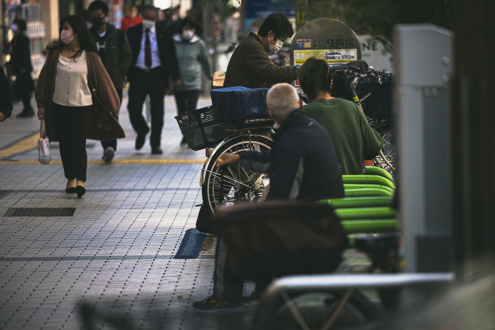 「新宿の歩道脇にある駐輪場とベンチに座る人たち」の写真