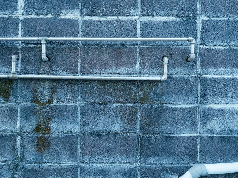 ブロック塀からのびる配管の写真