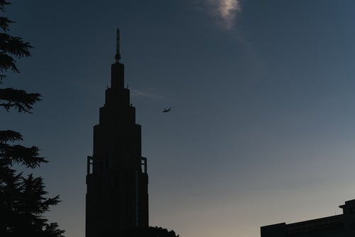 青空に映る時計台と飛行機のシルエットの写真