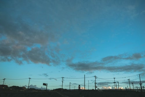 電柱のシルエットと薄雲かかる青空の写真