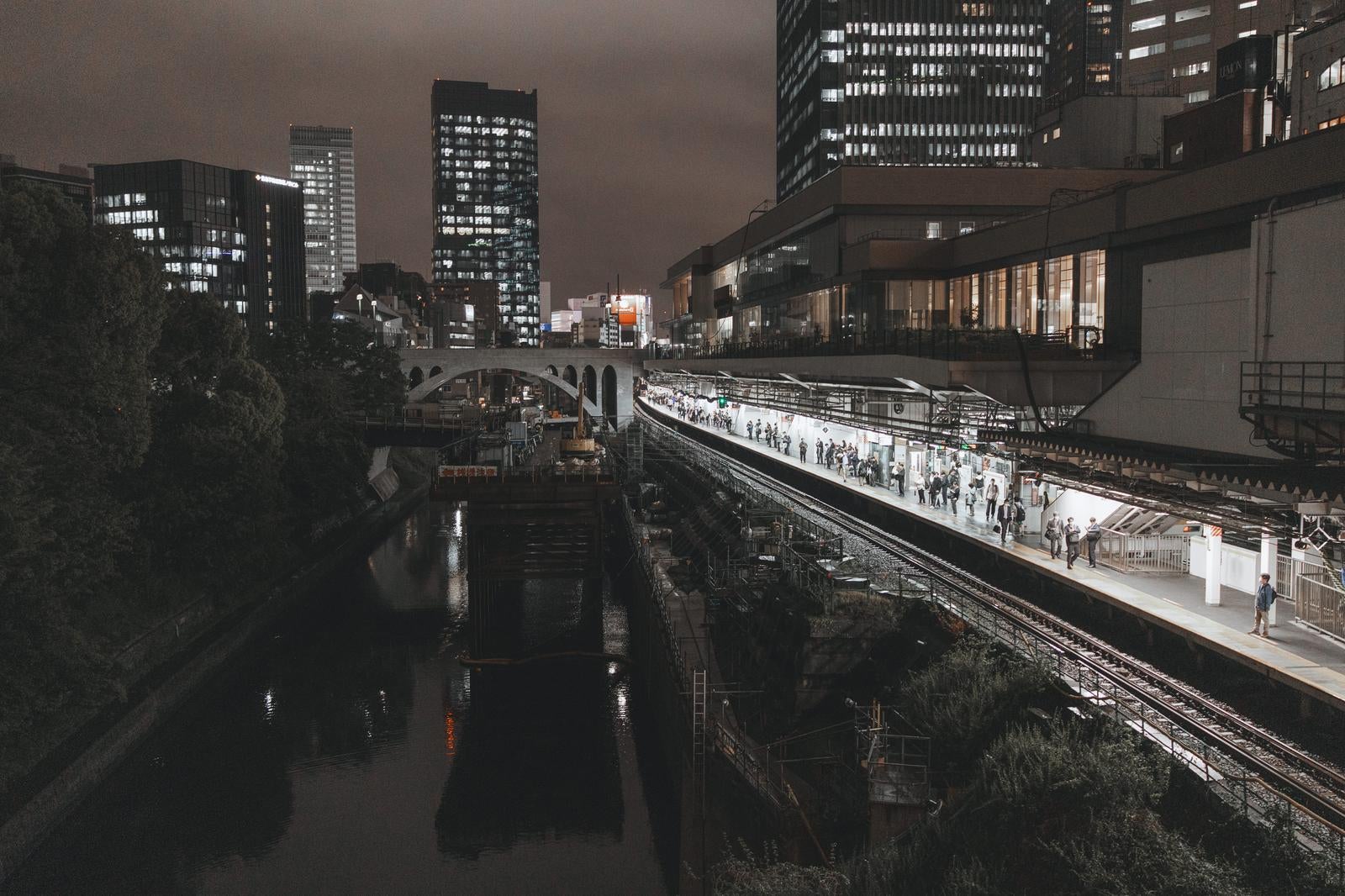 夜の御茶ノ水駅ホームに立つ乗客と隣を流れる神田川、周囲の高層ビル群