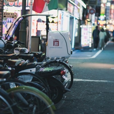 路地に駐車した二輪と繁華街の灯りの写真