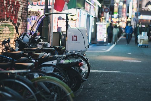 路地に駐車した二輪と繁華街の灯りの写真
